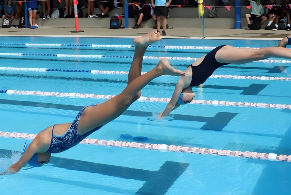 Ein Schwimmer in schwarzem Badeanzug taucht im Schwimmbecken auf dem Gelände der Toormina High School ein.
