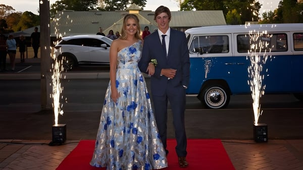 Ein Paar in formeller Kleidung steht auf dem roten Teppich vor einem alten blauen Van auf dem Campus der Toowoomba Anglican School.