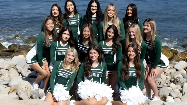 Eine Gruppe von Cheerleaderinnen der Torrance South High School posiert gemeinsam an einer felsigen Küste mit dem Ozean im Hintergrund.
