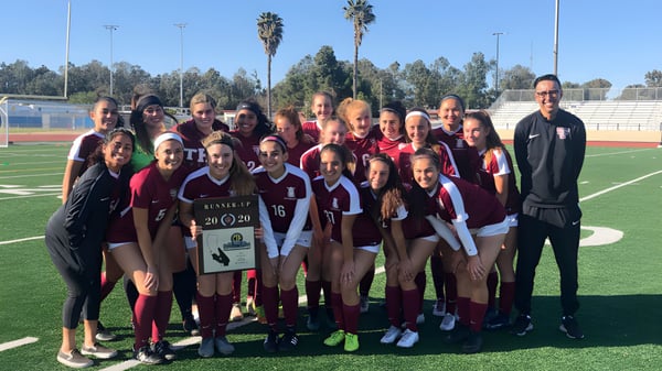 Eine Gruppe junger Fußballspielerinnen und ihr Trainer stehen zusammen auf dem Fußballfeld der Torrance Unified School District.
