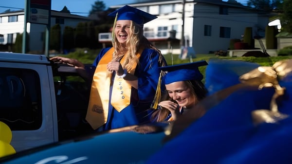 Eine lächelnde Absolventin in blauem Talar steht neben einem Auto auf dem Campus des Torrance Unified School District mit weiteren Absolventen.