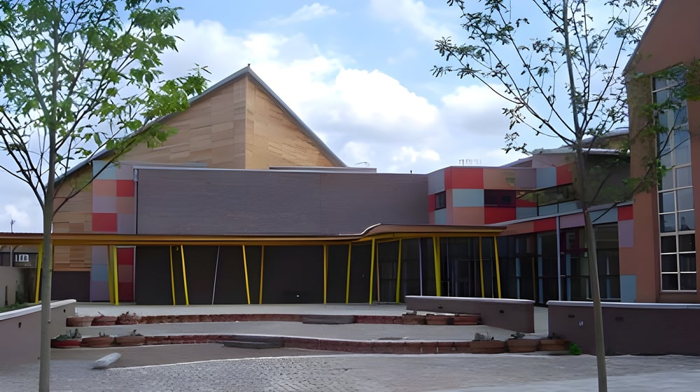 Das moderne Gebäude mit dreieckigem Dach auf dem Campus der Townley Grammar School ist von Bäumen und einem gepflasterten Bereich umgeben.