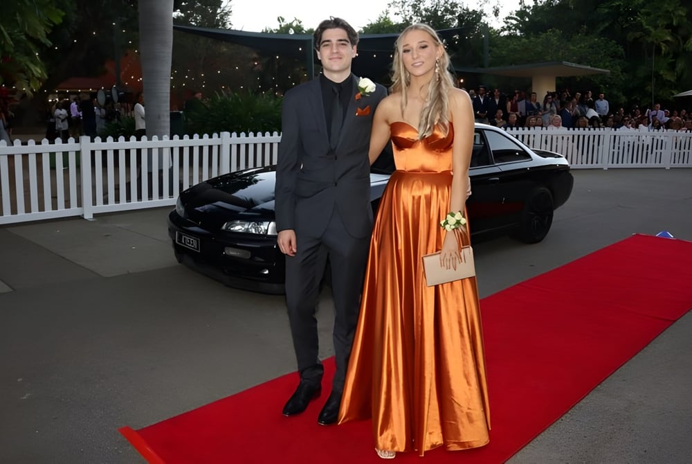Eine Schülerin und ein Schüler der Townsville Grammar School stehen in formaler Kleidung auf dem roten Teppich vor einem schwarzen Auto.