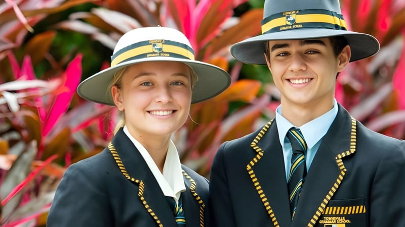 Zwei Schülerinnen der Townsville Grammar School tragen traditionelle Hüte und Uniformen vor einem farbenfrohen Hintergrund.