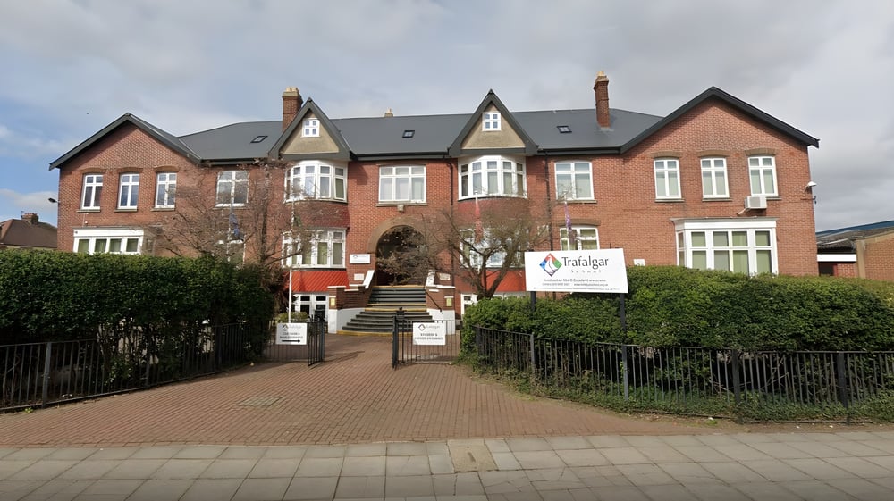 Das mehrstöckige Backsteingebäude mit Rundbogenfenstern und Ziegeldach steht auf dem Campus der Trafalgar School.