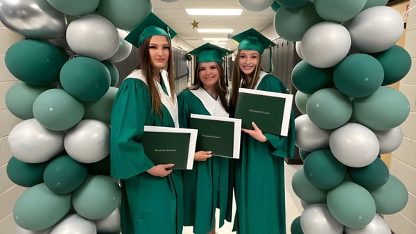 Eine Gruppe junger Frauen in grünen Abschlusskleidern und Hüten beim Abschlussfoto auf dem Campus der Transcona Collegiate.