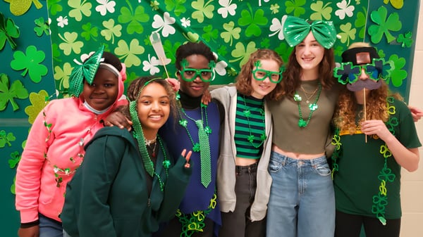 Eine Gruppe von Schülerinnen und Schülern der Transcona Collegiate trägt festliche grüne Kleidung mit Kleeblattmotiven vor dekoriertem Hintergrund.