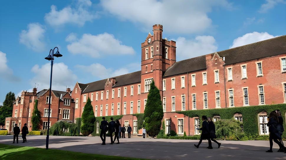 Das historische Gebäude mit hohem Turm auf dem Campus des Trent College ist von Bäumen umgeben und zeigt Menschen auf dem Weg.
