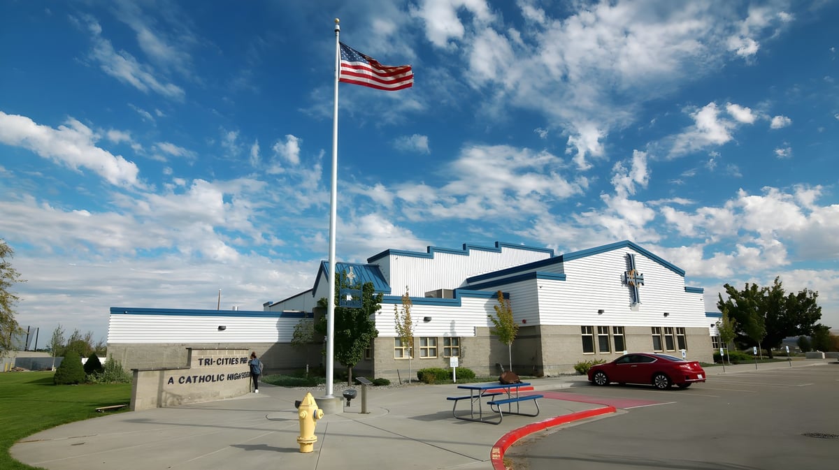 Eine große amerikanische Flagge weht über dem modernen Gebäude der Tri-Cities Prep Catholic High School mit rotem Teppich und grüner Wiese.