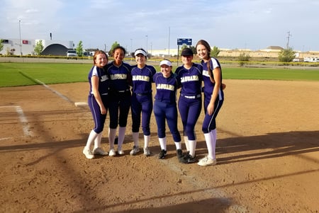 Eine Gruppe weiblicher Softballspielerinnen steht auf dem Spielfeld der Tri-Cities Prep Catholic High School.