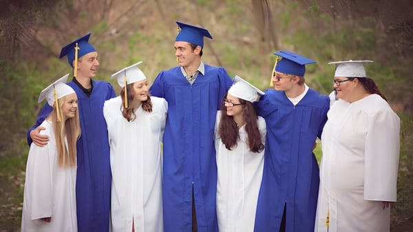 Eine Gruppe Absolventen in blauen und weißen Talaren steht auf dem Außengelände der Tri-State Christian School vor bewaldetem Hintergrund.