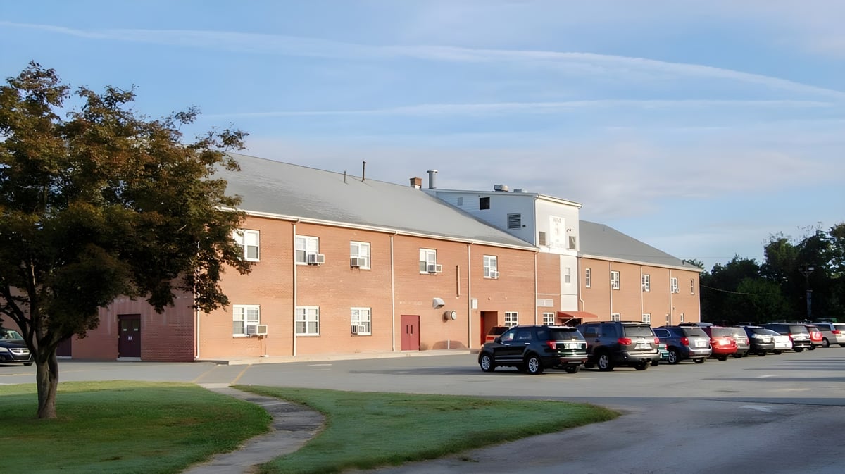 Das Backsteingebäude der Tri-State Christian School ist umgeben von Bäumen und einer Grünfläche mit einem Parkplatz im Vordergrund.