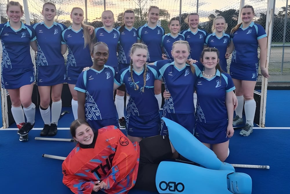 Eine Gruppe junger Athletinnen in blauen Uniformen auf dem Sportplatz der Trident High School posiert vor einem großen aufblasbaren Gegenstand.