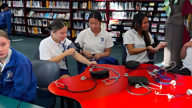 Schüler der Trident High School untersuchen medizinische Geräte und Materialien in einem Klassenraum mit Bücherregalen.