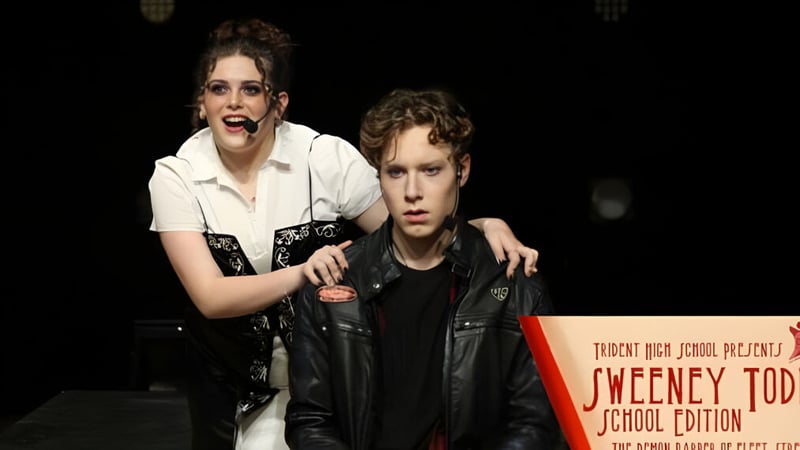 Eine Frau und ein Mann stehen vor einem Schild mit der Aufschrift Trident High School.