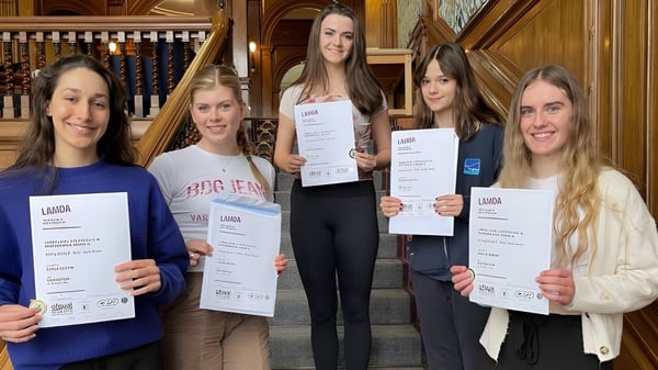 Fünf Schülerinnen der Tring Park School for the Performing Arts halten in einem historischen Raum ihre Diplome in die Kamera.