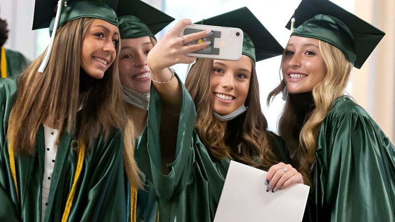 Vier Schülerinnen der Trinity Bay State High School machen gemeinsam in grünen Abschlussgewändern ein Selfie nach der Abschlussfeier.