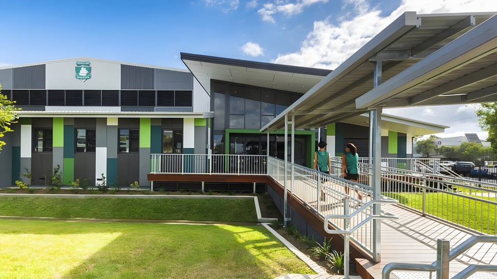 Das moderne mehrstöckige Gebäude der Trinity Bay State High School ist von einer Wiese und einem Weg mit Geländern umgeben.