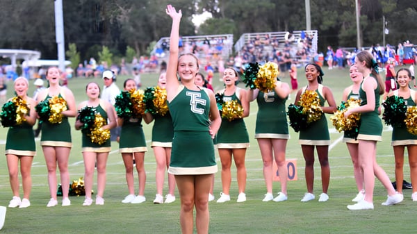 Cheerleader in grünen Uniformen mit goldenen Pompons stehen auf dem Sportfeld der Trinity Catholic High School.
