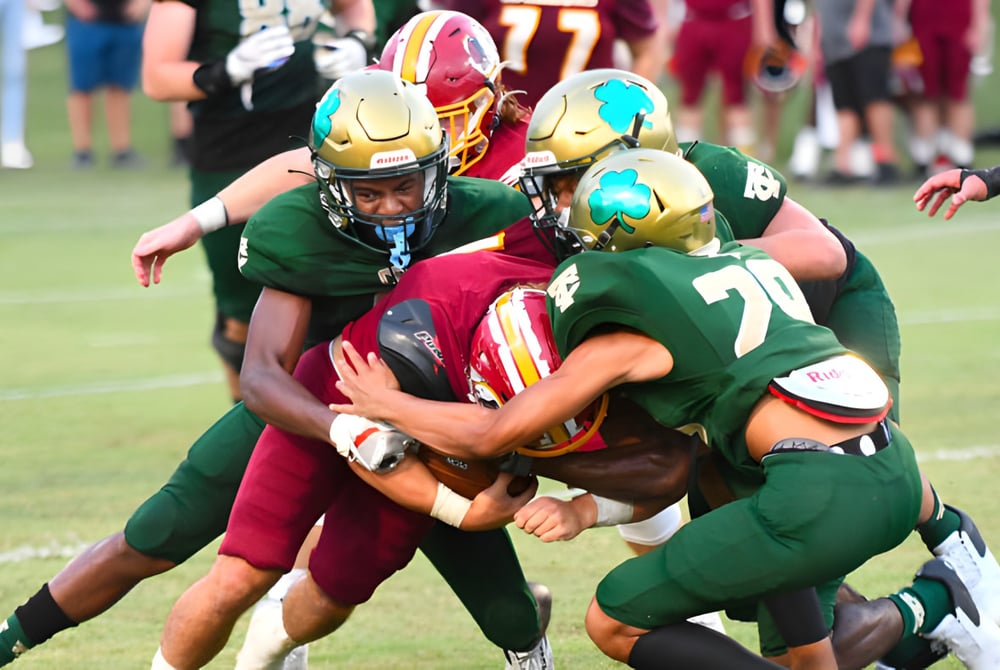Schüler der Trinity Catholic High School führen auf dem Spielfeld eine intensive Football-Tackle-Szene aus.