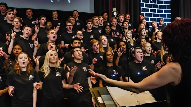 Eine große Gruppe von Schülerinnen und Schülern der Trinity Catholic High School steht auf einer Bühne vor einer Backsteinwand.