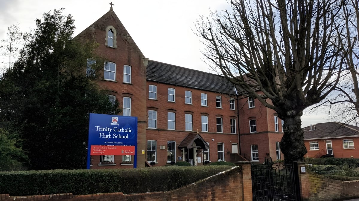 Das Backsteingebäude mit einem Türmchen auf dem Campus der Trinity Catholic High School steht von Bäumen und einem Zaun umgeben.