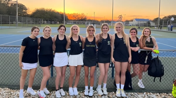 Eine Gruppe junger Tennisschülerinnen posiert auf dem Tennisplatz der Trinity Catholic High School bei Sonnenuntergang.