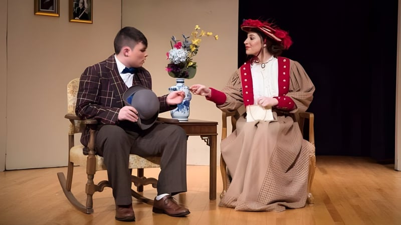 Ein Mann in einem Schaukelstuhl und eine Frau mit einem Blumenvasen sind in historischen Kostümen auf dem Campus der Trinity Catholic Jr/Sr High School zu sehen.