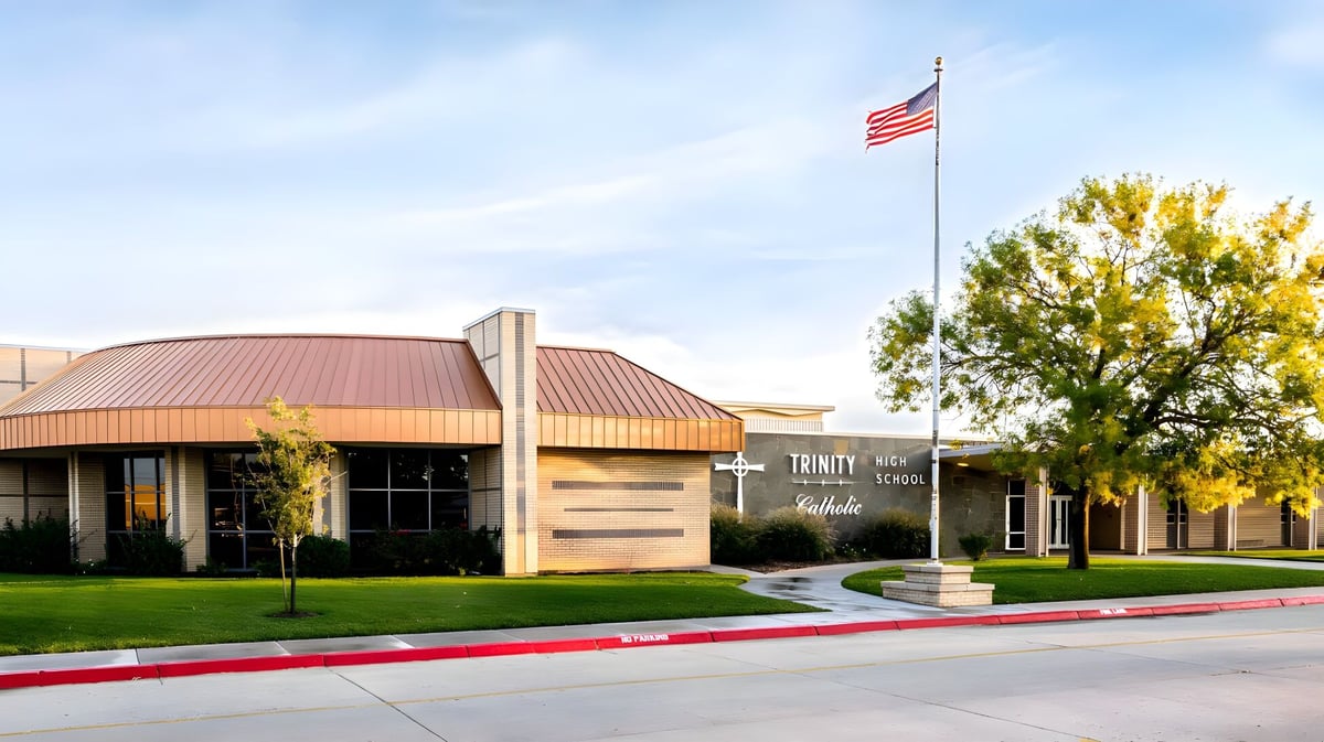 Das eingeschossige Gebäude mit rotem Metall-Dach auf dem Gelände der Trinity Catholic Jr/Sr High School ist von Rasen und Bäumen umgeben.