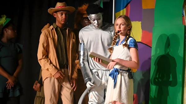 Schüler der Trinity Christian Academy posieren in bunten Theaterkostümen vor einem farbenfrohen abstrakten Hintergrund.