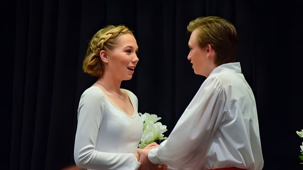 Ein junges Paar steht in formeller Kleidung auf der Bühne der Trinity Christian School vor einem dunklen Vorhang.