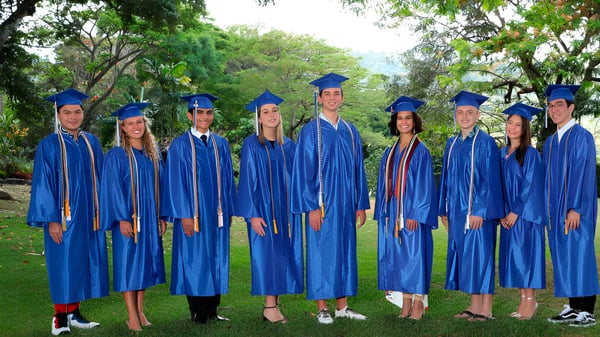 Eine Gruppe von Absolventen der Trinity Christian School steht in blauen Talaren im grünen Außenbereich.