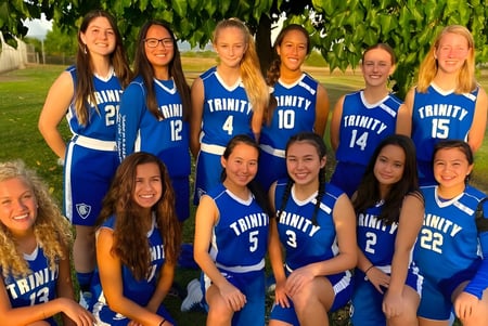 Eine Gruppe junger Schülerinnen in blauen Sportuniformen posiert gemeinsam im Freien auf dem Gelände der Trinity Christian School.