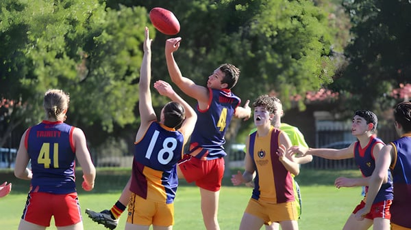 Schüler des Trinity College spielen Australian Football auf einem Grasfeld mit grüner Umgebung.