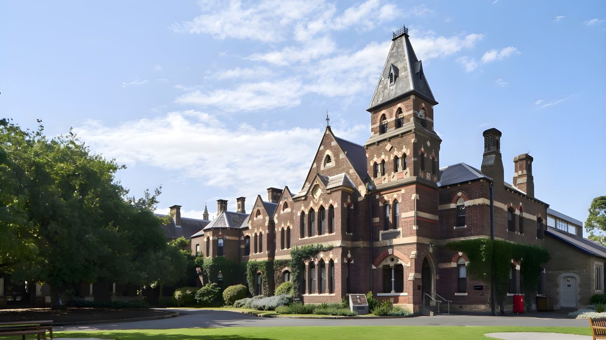 Das historische Backsteingebäude mit hohem Turm auf dem Campus des Trinity College ist von grünen Bäumen umgeben.