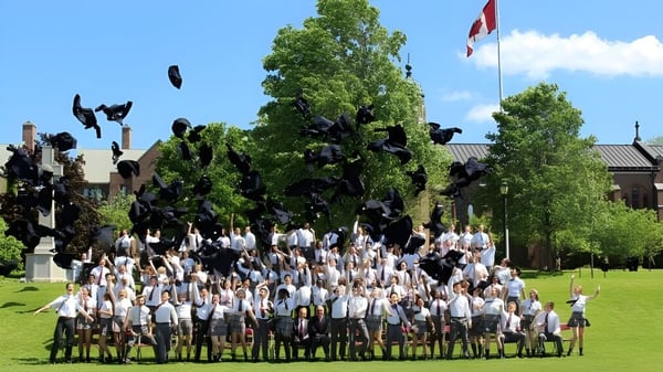 Eine Gruppe von Absolventinnen und Absolventen in weißen Talaren und Hüten versammelt sich auf dem Rasen des Trinity College School.