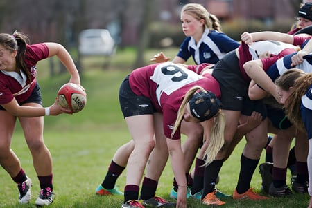 Eine Gruppe von Rugbyspielerinnen der Trinity College School steht in einem Gedränge auf einem grasbewachsenen Spielfeld.