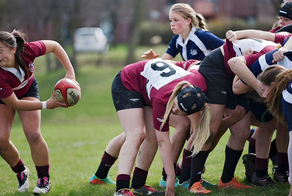 Eine Gruppe von Rugbyspielerinnen der Trinity College School steht in einem Gedränge auf einem grasbewachsenen Spielfeld.