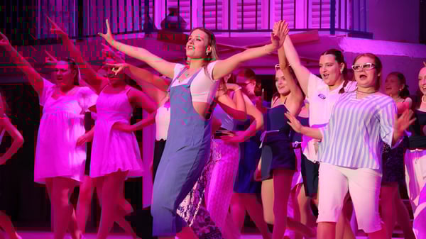 Eine Gruppe von Schülerinnen und Schülern tanzt auf der Bühne des Trinity College vor lebendiger pink-violetter Beleuchtung.