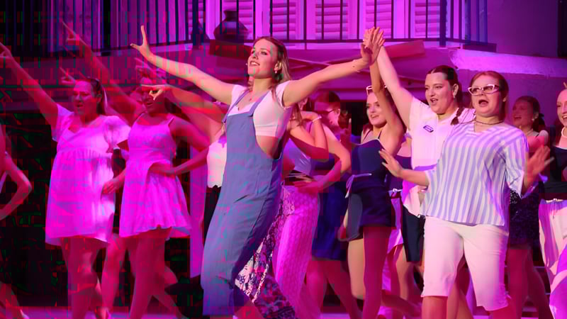 Eine Gruppe von Schülerinnen und Schülern tanzt auf der Bühne des Trinity College vor lebendiger pink-violetter Beleuchtung.