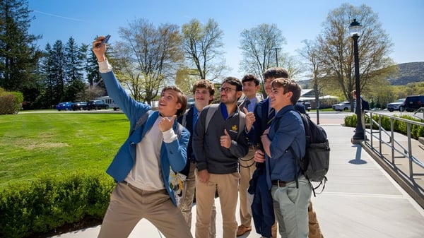 Eine Gruppe Schüler steht an einem sonnigen Tag auf dem Außengelände der Trinity-Pawling School mit Wiese und Bäumen im Hintergrund.