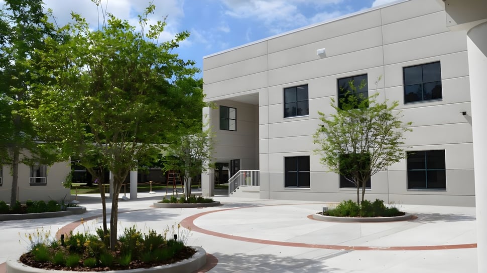 Das moderne mehrstöckige Gebäude der Trinity Preparatory School mit großen Fenstern und einem begrünten Innenhof mit Wegen und Pflanzen.