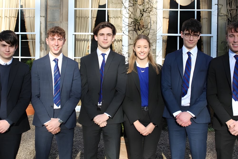 Eine Gruppe Jugendlicher steht vor einem Gebäude auf dem Campus der Trinity School.