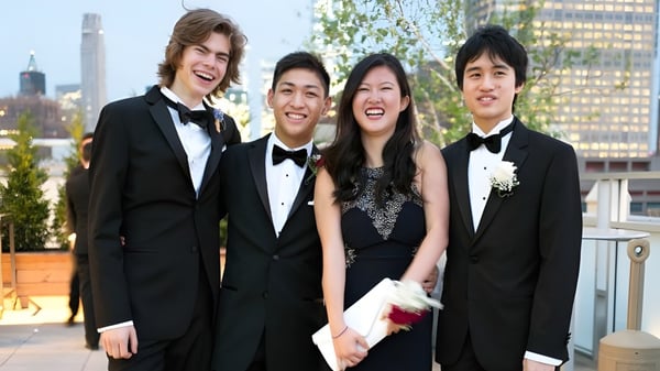 Vier Schüler der Trinity School posieren vor einer Stadtlandschaft mit hohen Gebäuden.