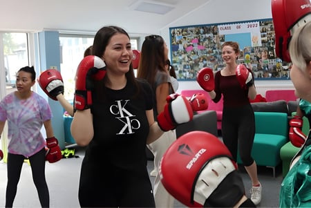 Schülerinnen der Truro High School for Girls trainieren gemeinsam mit Boxhandschuhen und Kopfschutz im Trainingsraum.