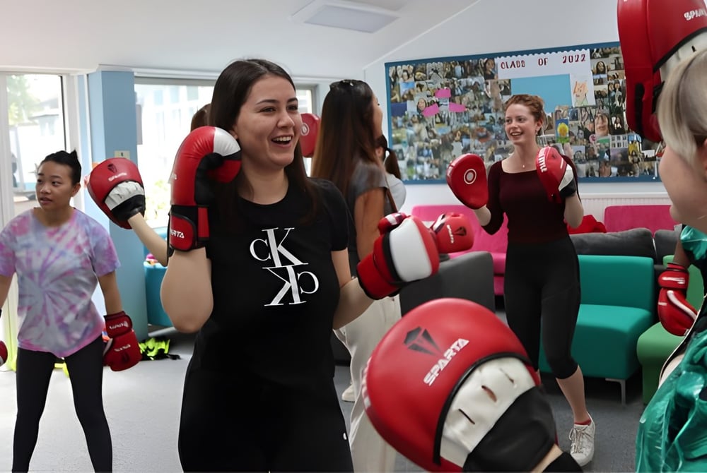 Schülerinnen der Truro High School for Girls trainieren gemeinsam mit Boxhandschuhen und Kopfschutz im Trainingsraum.
