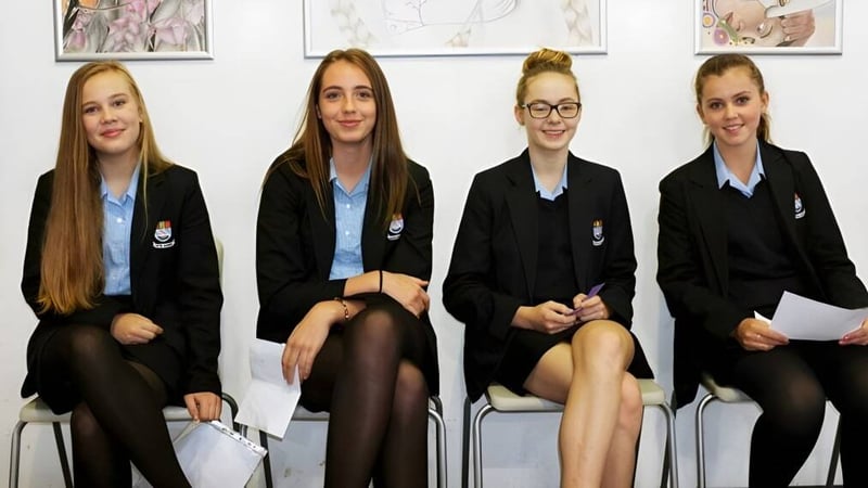 Vier Schülerinnen der Truro High School for Girls sitzen im Klassenzimmer vor gerahmten Kunstwerken an der Wand.