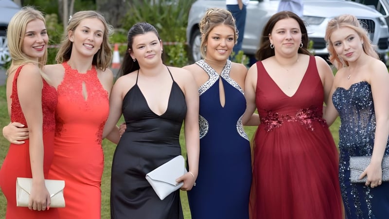 Sechs Schülerinnen der Truro High School for Girls posieren in eleganten Abendkleidern zusammen im Freien vor grünem Hintergrund.