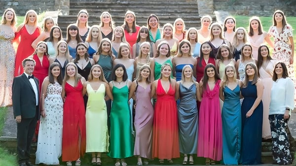 Eine große Gruppe von Frauen in bunten Kleidern steht vor einem Steingebäude auf dem Campus der Tudor Hall School.