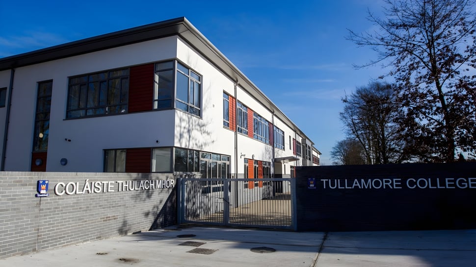 Das moderne mehrstöckige Gebäude des Tullamore College ist von Bäumen umgeben unter einem klaren blauen Himmel.
